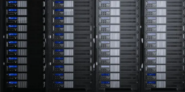 This photograph depicts a densely packed server rack in a dark room, showcasing numerous computer systems with grey and blue components.
