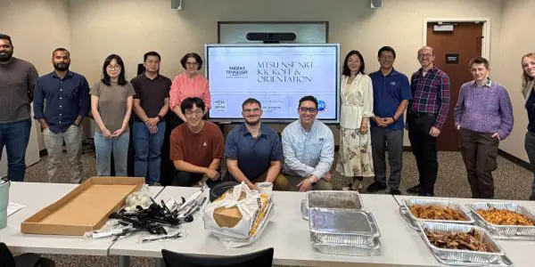 A group of 13 MTSU students and faculty pose in a line in front of a table of food