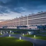 A vast illuminated data center facility at twilight with wind turbines on the horizon