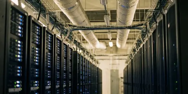 Long data centre aisle between rows of server racks with blue lights and overhead ducts