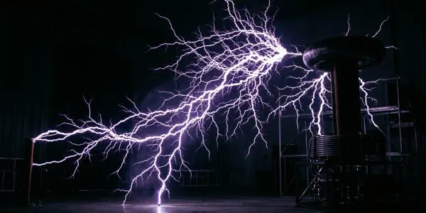A dramatic display of purple and white electrical arcs crackle between metal structures in a darkened room