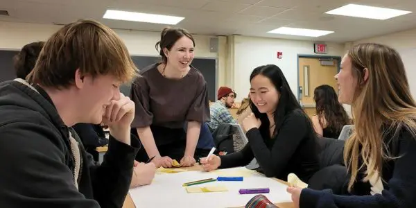 An instructor leans on a table to share something with four students