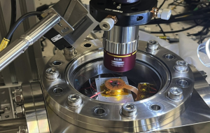 A sophisticated scientific instrument is shown, positioned within a metallic enclosure and illuminated with bright, contrasting colours.