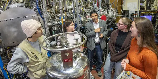 Five researchers meeting in a lab with large metallic instruments