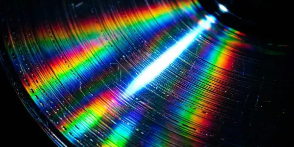 A close-up of a circular disc displays vibrant rainbow colours reflecting light against a dark background
