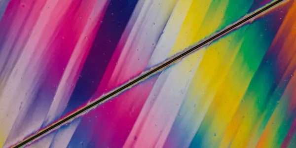 A macro shot reveals vibrant, swirling colours within a transparent material, likely a crystal or liquid, against a black background.