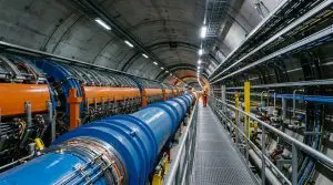 A long, blue cylindrical structure dominates a concrete tunnel, illuminated by bright overhead lights and accented with orange and silver