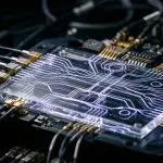 A complex microchip with glowing circuitry sits amidst a dark, metallic framework, illuminated by cool, blue light