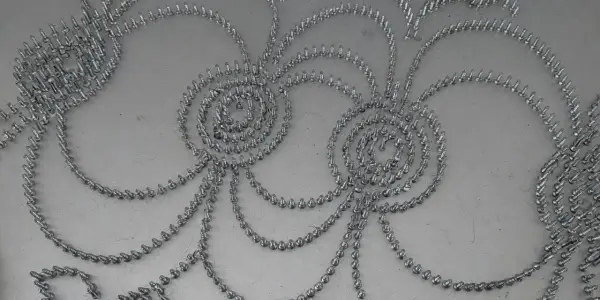 A grayscale overhead view displays a complex, swirling pattern of small metallic spheres on a light surface.