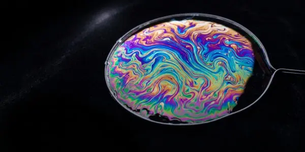 Soap film on a wire loop swirling with iridescent purple, blue, green and gold bands