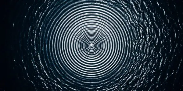 Concentric ripples expand across dark blue water, creating a hypnotic spiral pattern with bright highlights