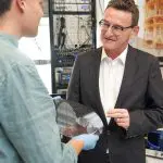 A 300mm silicon wafer of Diraq spin-qubit devices held in the laboratory, with measurement racks behind