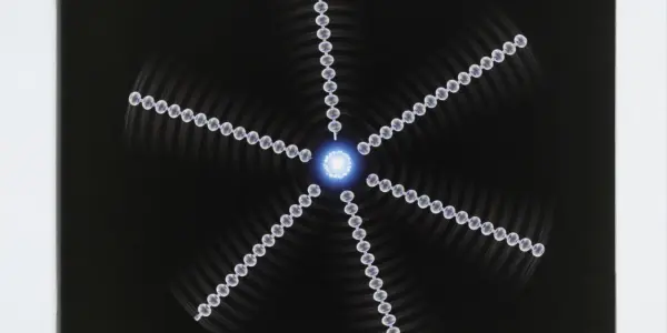 A dark studio setting features a symmetrical, glowing blue and white pattern resembling a starburst or expanding energy waves.