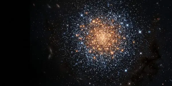 A dense, spherical cluster of stars glows golden against a backdrop of distant galaxies and faint blue starlight.