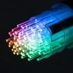 Glowing rainbow optical fiber strands bundled inside a transparent connector against a black background.