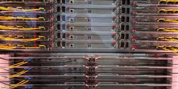 A server rack filled with densely packed computing hardware dominates the frame, illuminated by cool, artificial light