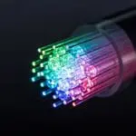 A bundle of optical fibers glowing in rainbow colors emerging from the end of a dark cable.