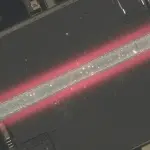 A microchip with a central, glowing red structure is visible under a microscope, set against a dark background.
