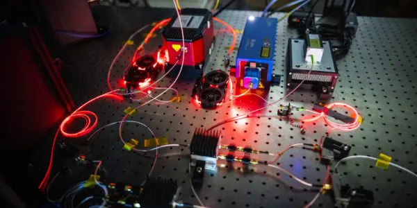 This photograph shows a complex optical experiment setup on a reflective table with numerous lasers and fiber optic cables.