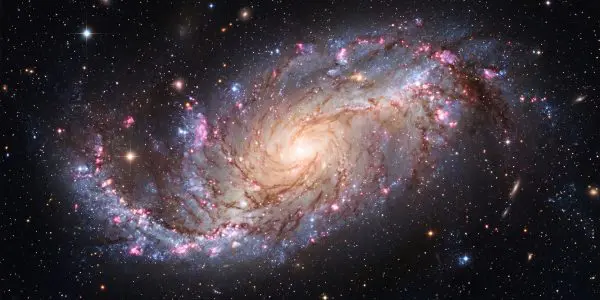 This stunning image showcases a spiral galaxy, Messier 83, with swirling arms of pink, blue, and orange gas and dust.