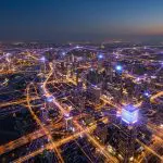 aerial dusk view of a city laced with glowing purple network links between rooftops