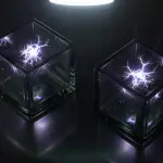 Two transparent cubes containing bright, branching energy patterns sit on a reflective surface, illuminated by a light above.