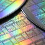 A close-up reveals iridescent silicon wafers against a dark background, displaying intricate grid patterns and rainbow hues