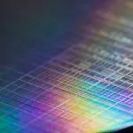 A close-up shot reveals a silicon wafer with intricate circuit patterns, reflecting a vibrant rainbow of colors against a dark background.