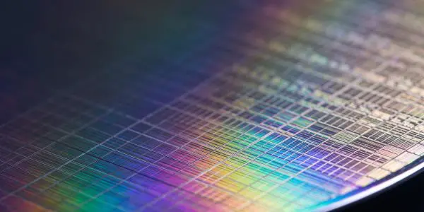 A close-up shot reveals a silicon wafer with intricate circuit patterns, reflecting a vibrant rainbow of colors against a dark background.
