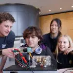 A group of high school students inspect a quantum sensor with a man at an expo booth
