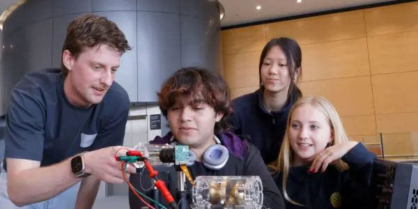 A group of high school students inspect a quantum sensor with a man at an expo booth