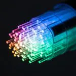 Glowing rainbow optical fiber strands bundled inside a transparent connector against a black background.