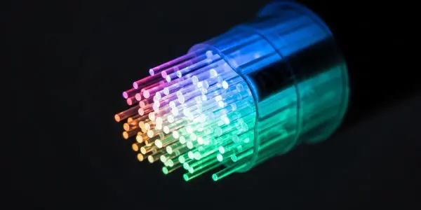 Glowing rainbow optical fiber strands bundled inside a transparent connector against a black background.