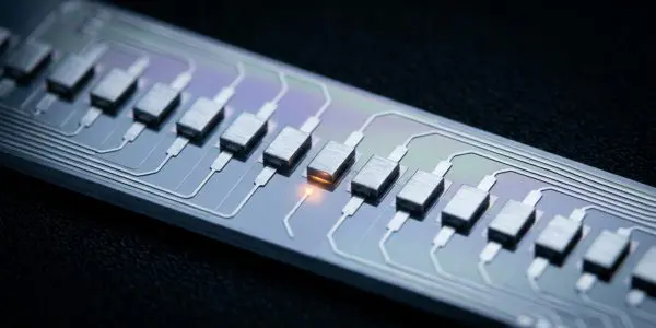 A close view along a silicon chip showing a row of gate electrodes with one active site glowing
