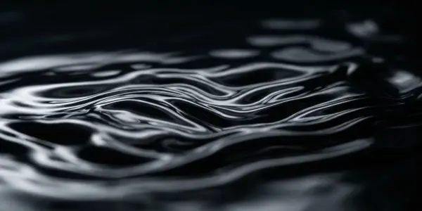 A close-up of dark, swirling liquid with bright white highlights creates an abstract, moody effect, dominated by black and grey.
