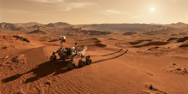 The Mars rover traverses a vast, orange desert landscape under a warm, golden sunset sky.