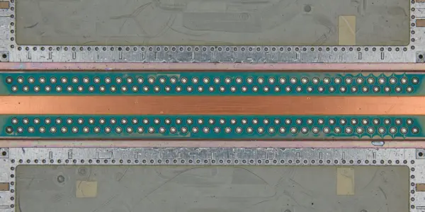 A close-up of a photonic chip with many circular holes, set against a black background, in shades of copper, grey and green.