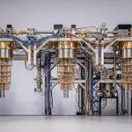A complex arrangement of metallic structures with numerous cables dominates a bright, clean laboratory setting