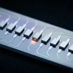 A close view along a silicon chip showing a row of gate electrodes with one active site glowing