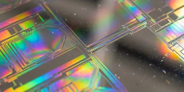 A close-up of a microchip's patterned surface displays iridescent colours, set against a dark background, creating a futuristic aesthetic.