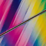 A macro shot reveals vibrant, swirling colours within a transparent material, likely a crystal or liquid, against a black background.