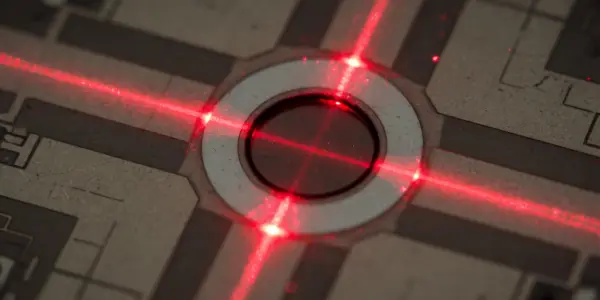 A microchip with a central circular feature illuminated by bright red laser beams against a dark background.