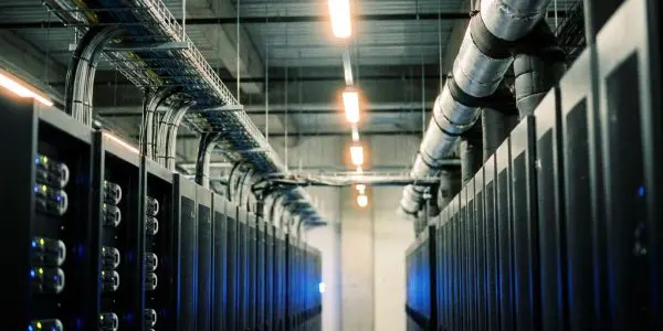 A long corridor of server racks fills the frame, illuminated by cool blue lights and overhead fluorescent fixtures.