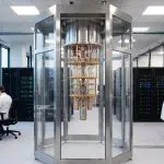 A bright, modern laboratory features a large cylindrical structure surrounded by computer servers and workstations