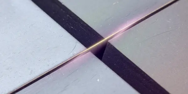 A close-up of four metallic blocks forming a cross-shape, with a bright pink line of light at the intersection, against a dark background.