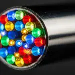 Close-up end view of a metal cable packed with red, blue, green and yellow glowing optical fibers.