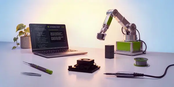 A robotic arm sits on a dark table with a laptop, tools and wires, illuminated by a soft, warm light.