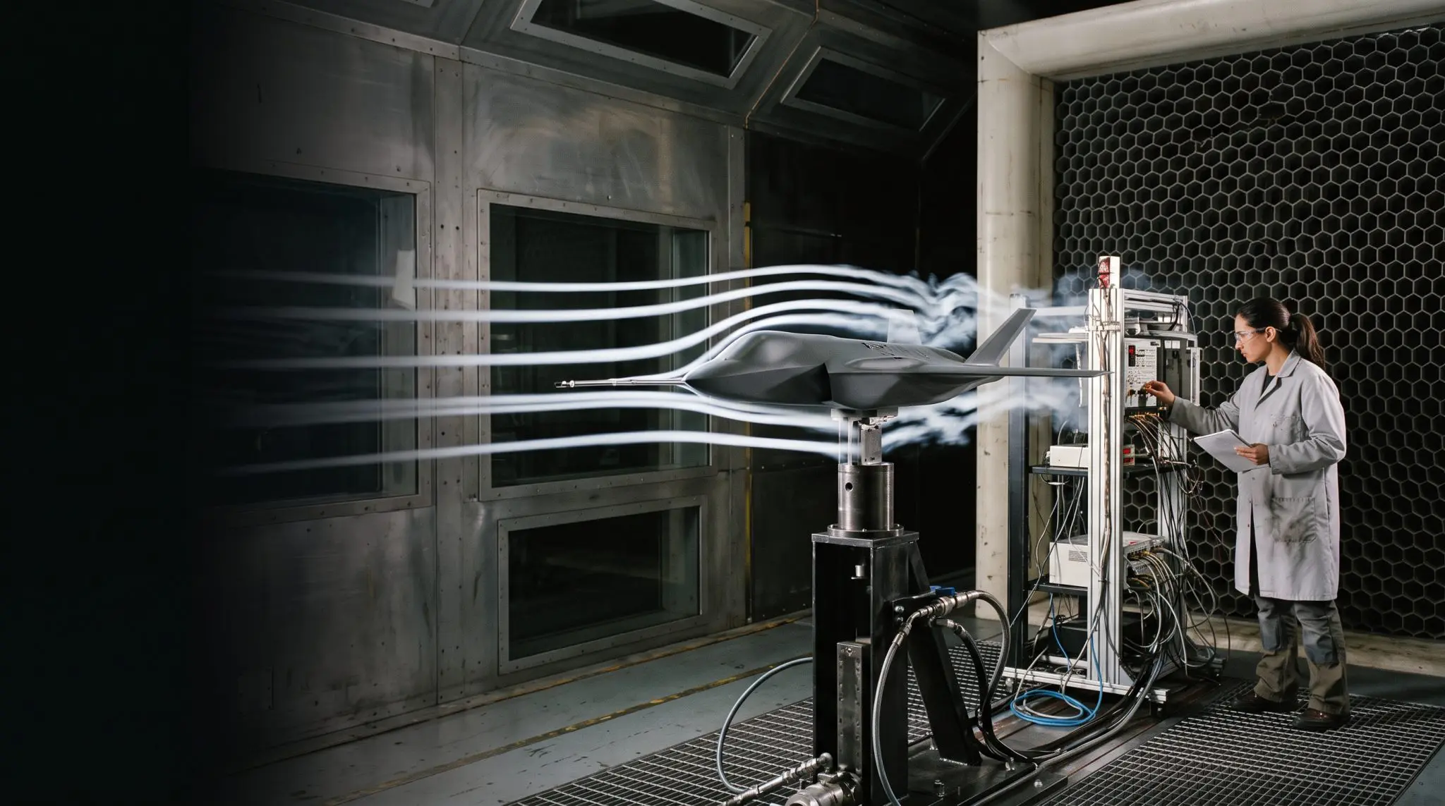 A dark wind tunnel test reveals airflow around a dark, streamlined model, with a scientist monitoring equipment nearby.