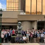 Conference attendees pose for a group photo outside a hotel