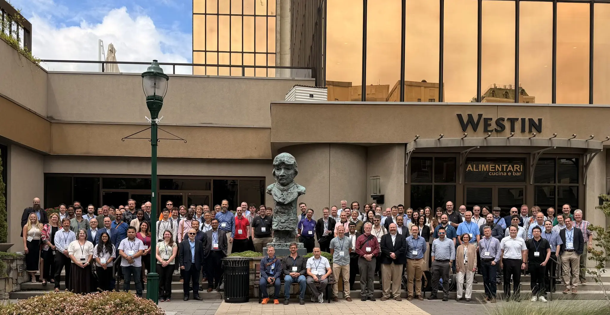 Conference attendees pose for a group photo outside a hotel